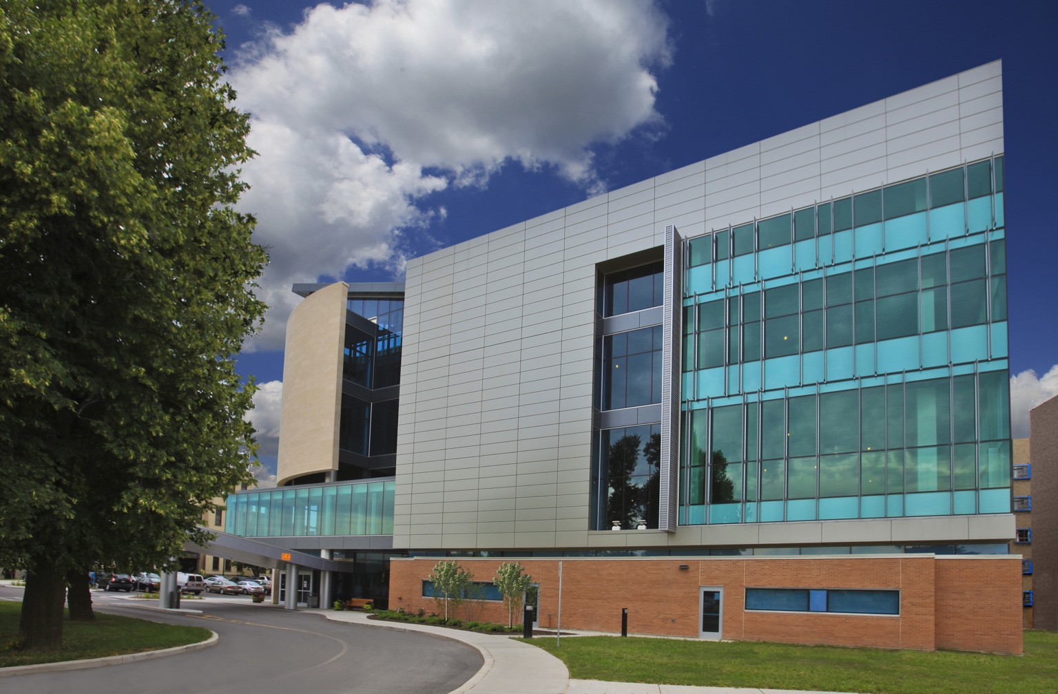 Modern building with pale metal cladding, turquoise glazing, and a curved entrance drive.