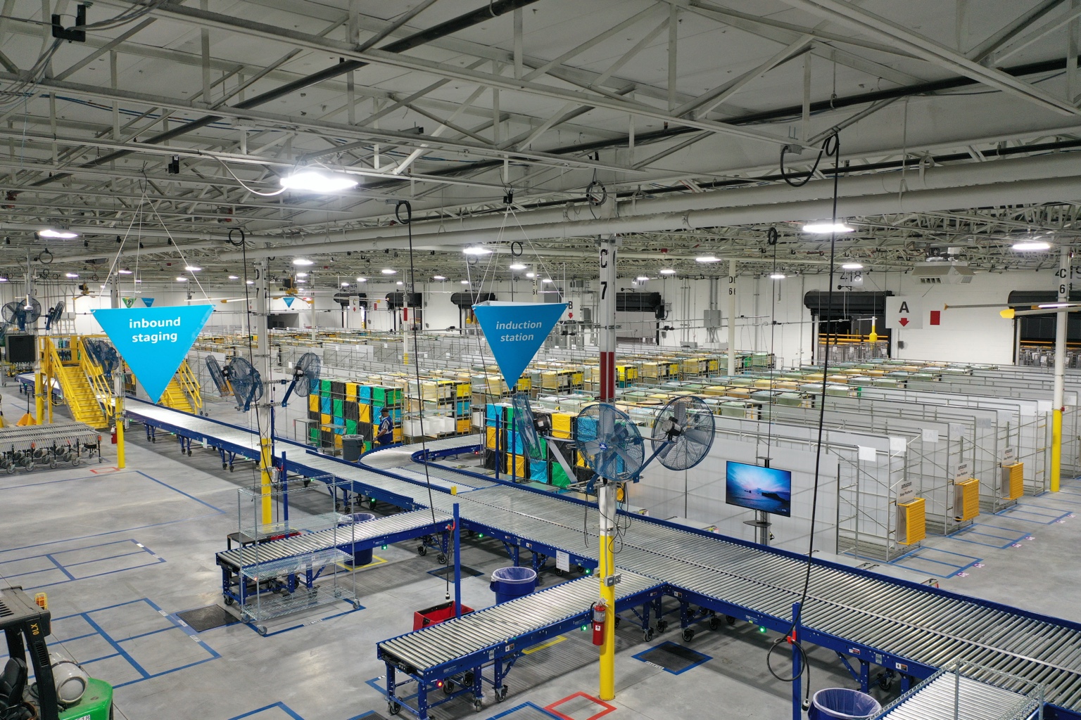 Interior of a distribution facility with roller conveyors, sorting stations, and overhead steel framing.