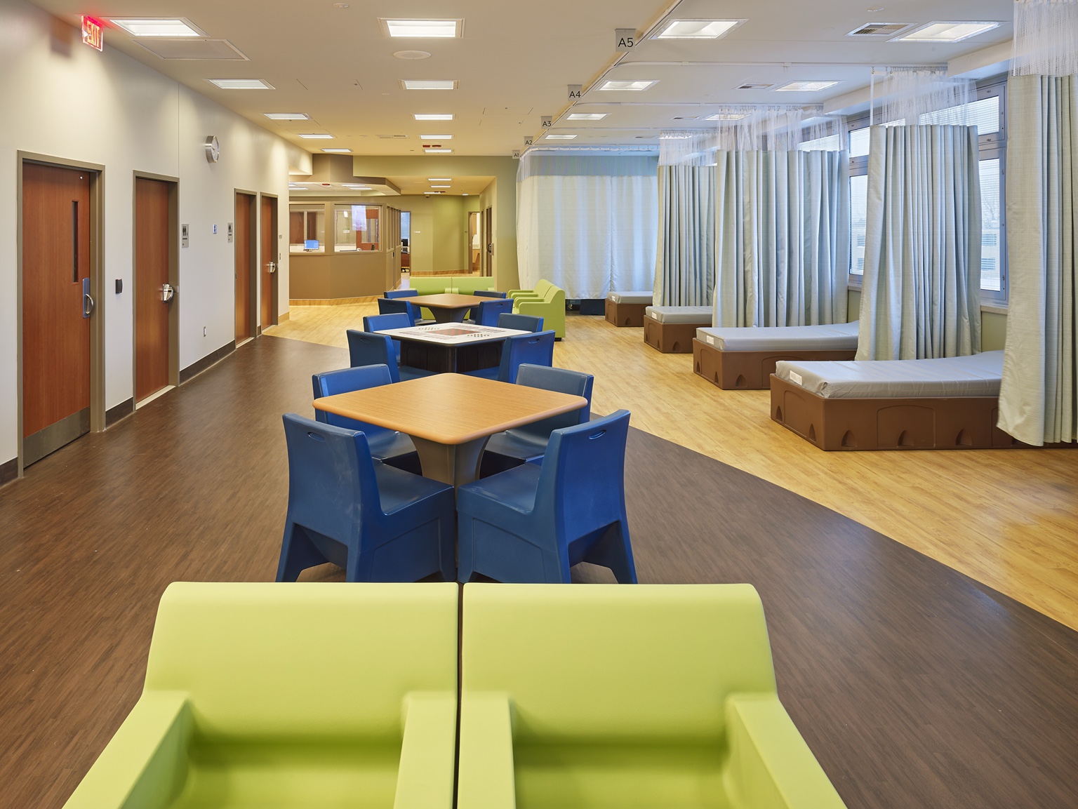 Treatment-room interior with curtained patient bays, tables, and colorful seating.