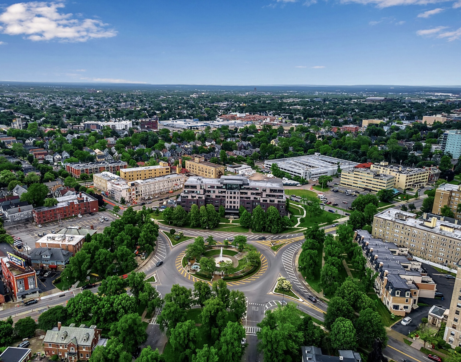 Aerial view of a landscaped traffic circle and surrounding buildings in an urban neighborhood.